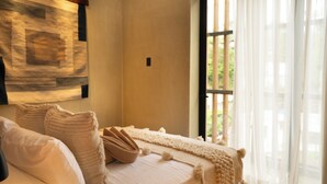 A neatly made bed with a beige blanket and pillows, a wooden headboard, and a window with sheer curtains.
