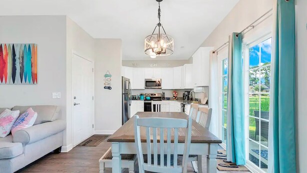 Una cocina moderna con armarios blancos, un comedor con mesa y sillas de madera, y vista a un jardín a través de amplios ventanales.