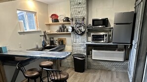 Uma cozinha com ilha central, banquetas, micro-ondas, geladeira e janela.