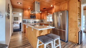 A kitchen with wooden cabinets, a stainless steel refrigerator, and a central island with stools. - Sierra National Forest & Yosemite Estate + Orchard Retreat (Oakhurst)