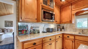 A kitchen with wooden cabinets, a microwave, and a countertop with various items. - Sierra National Forest & Yosemite Estate + Orchard Retreat (Oakhurst)
