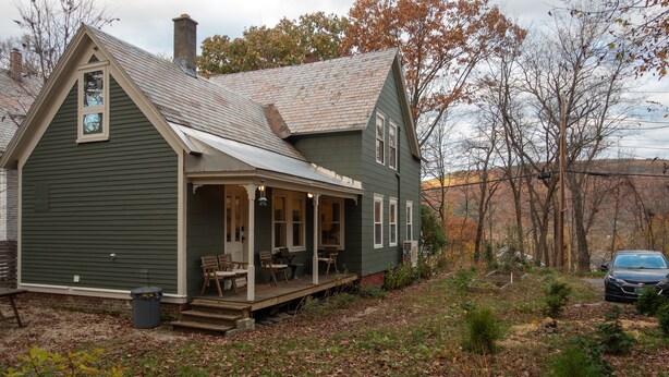 A green house with a porch, a chimney, and a car parked nearby.