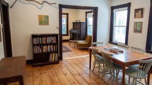 A dining area with a wooden table and chairs, a bookshelf, and a piano in the background.