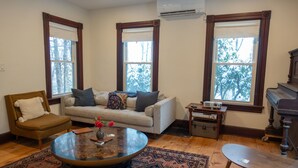 A living room with a sofa, armchair, coffee table, and a piano.