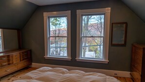 A bedroom with a large bed, two windows, a dresser, and a mirror.