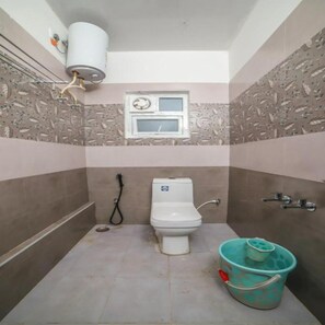 A small bathroom with a toilet, a window, and a water heater. - Blue Nile Suits By Indostay (Kotagiri)