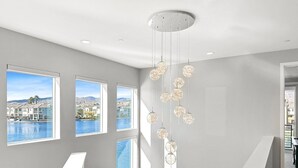 A modern interior with a white reception desk, large windows with a view of a body of water and buildings, and a hanging light fixture. - Casa Marina -15 min to Coachella (Indio)