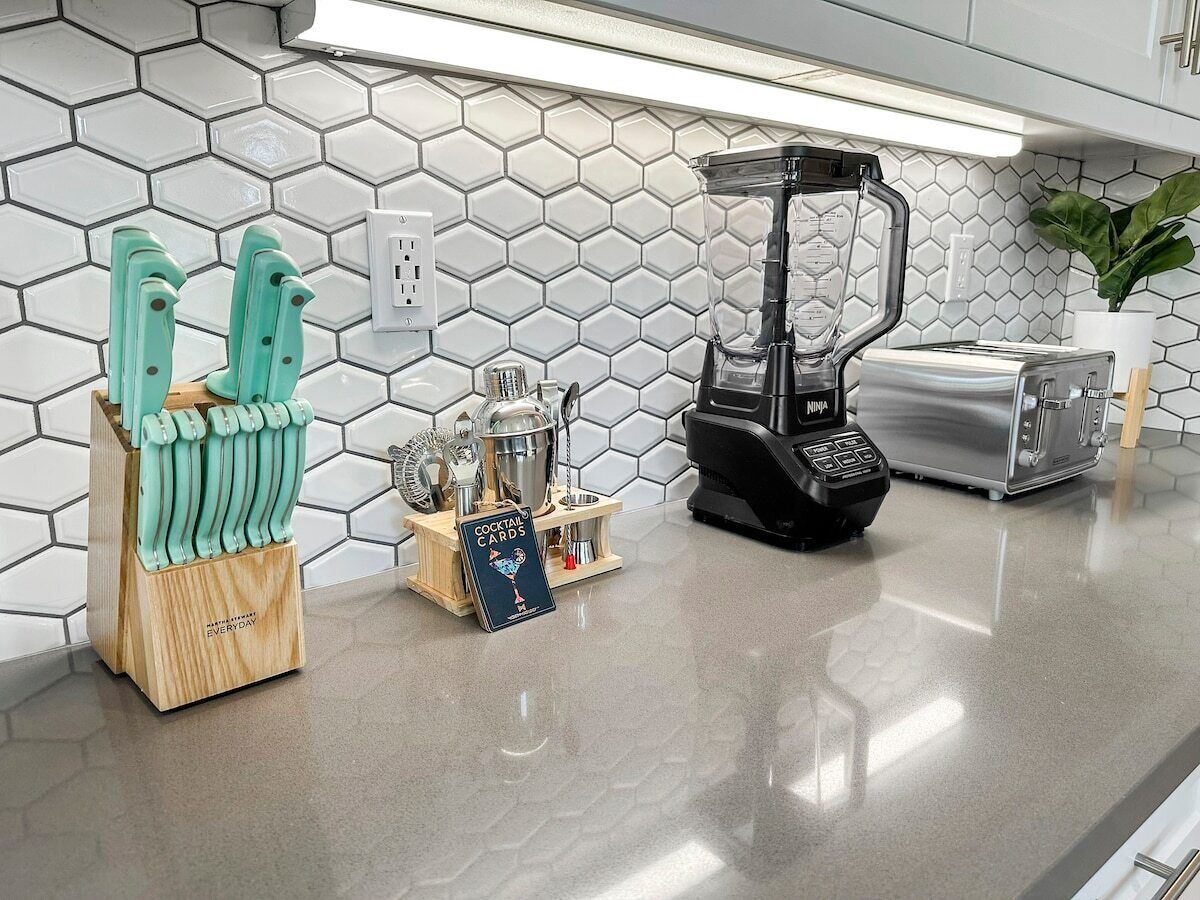 Une cuisine avec un dosseret de crédence en carreaux hexagonaux, un mixeur, un grille-pain et un bloc à couteaux en bois, ainsi qu’un présentoir à cocktails.
