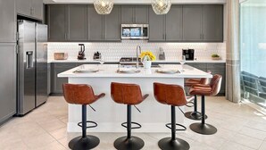 Une cuisine moderne avec des meubles gris, des appareils en acier inoxydable, un îlot central doté de tabourets, un éclairage suspendu et une grande fenêtre offrant une belle vue.