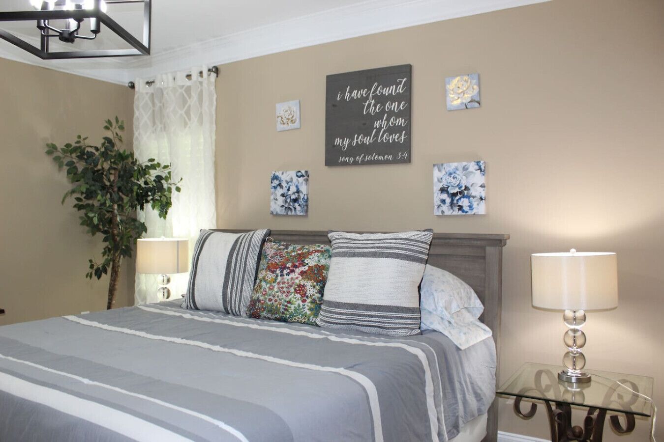 Una camera da letto con un letto, due lampade da comodino, un cartello appeso al muro e una pianta in vaso.