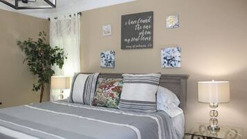 Una camera da letto con un letto, due lampade da comodino, un cartello appeso al muro e una pianta in vaso.