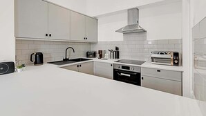 A modern kitchen with white cabinets, a stainless steel range hood, a built-in oven, and a toaster. - Contemporary Oasis in Paddington II (London)