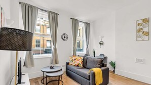 A living room with a sofa, a small round table, a lamp, and a clock on the wall. - Contemporary Oasis in Paddington II (London)