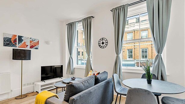 A modern living room with a sofa, a TV, a small table, and a dining area with chairs. - Contemporary Oasis in Paddington II (London)