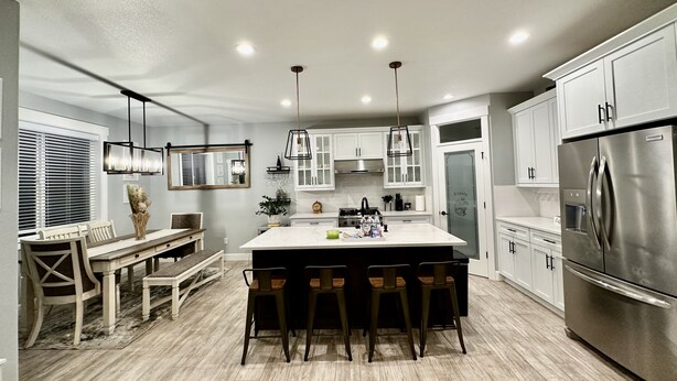 A modern kitchen with a central island, white cabinetry, stainless steel appliances, and a dining area with a bench and chairs. - House in West Salem (Salem)