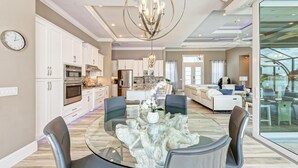 A modern kitchen with white cabinets, stainless steel appliances, and a dining area with a glass table and chairs. - Waterfront Luxury Retreat - Pool & Spa - Quick Harbor Access (Punta Gorda)