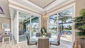 A spacious living room with a glass dining table, comfortable seating, and a large sliding glass door leading to a pool area. - Waterfront Luxury Retreat - Pool & Spa - Quick Harbor Access (Punta Gorda)
