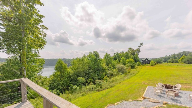 Une terrasse en bois avec une rambarde donnant sur une pelouse, où se trouvent un foyer et des chaises.