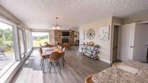 Une salle à manger spacieuse avec une longue table et des chaises, une cheminée et une vue dégagée grâce à de grandes fenêtres.