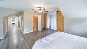 Une chambre spacieuse avec un grand lit, un ventilateur de plafond et une vue sur un couloir menant à la salle de bain.