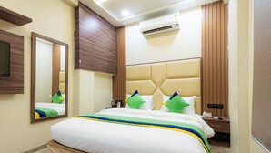 A hotel room with a large bed, a bedside table, a mirror, an air conditioning unit, and a window with curtains. - Treebo City Center (Nagpur)