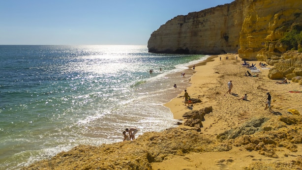 Une plage avec un ciel dégagé, une eau calme et des falaises rocheuses.