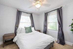 A bedroom with a bed, nightstands, a ceiling fan, and windows with curtains. - Cottage in Heart of Five Points - Pet Friendly! (Raleigh)