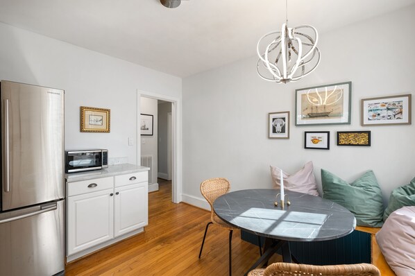 A modern kitchen with stainless steel appliances, a dining area with a round table, and a living space with a sofa and cushions. - Cottage in Heart of Five Points - Pet Friendly! (Raleigh)