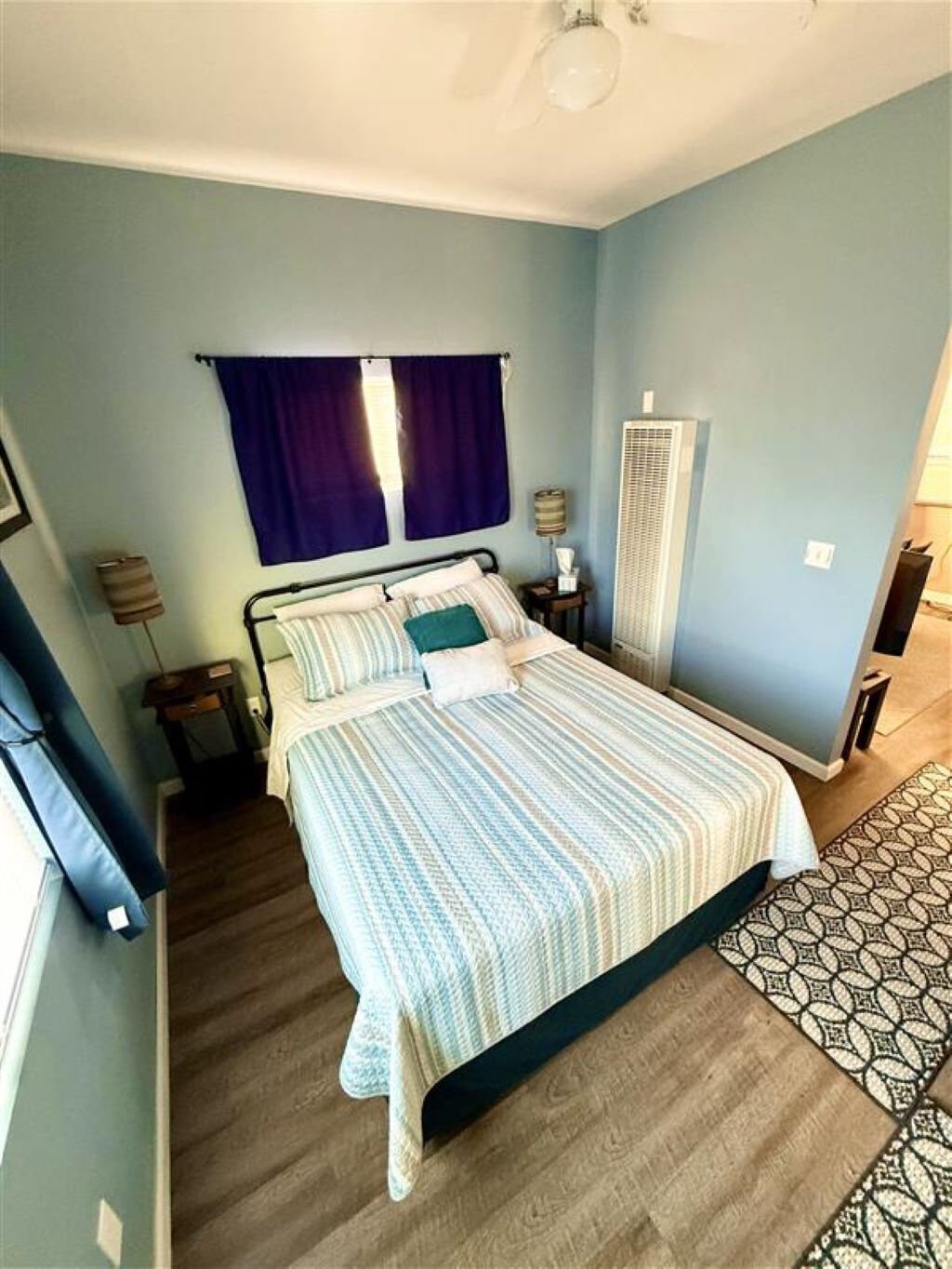 Een slaapkamer met een bed, gordijnen, een nachtkastje, een lamp en een radiator.