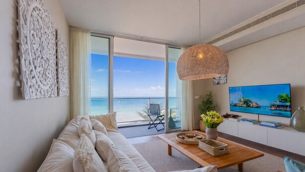 A modern living room with a large sofa, a wooden coffee table, and a TV on the wall. There is a balcony with a view of the ocean. - FLH Seaside Luxury at Madeira Palace Residence (Funchal)