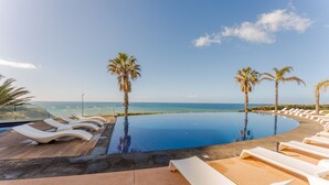An infinity pool with lounge chairs and palm trees, overlooking the ocean. - FLH Seaside Luxury at Madeira Palace Residence (Funchal)