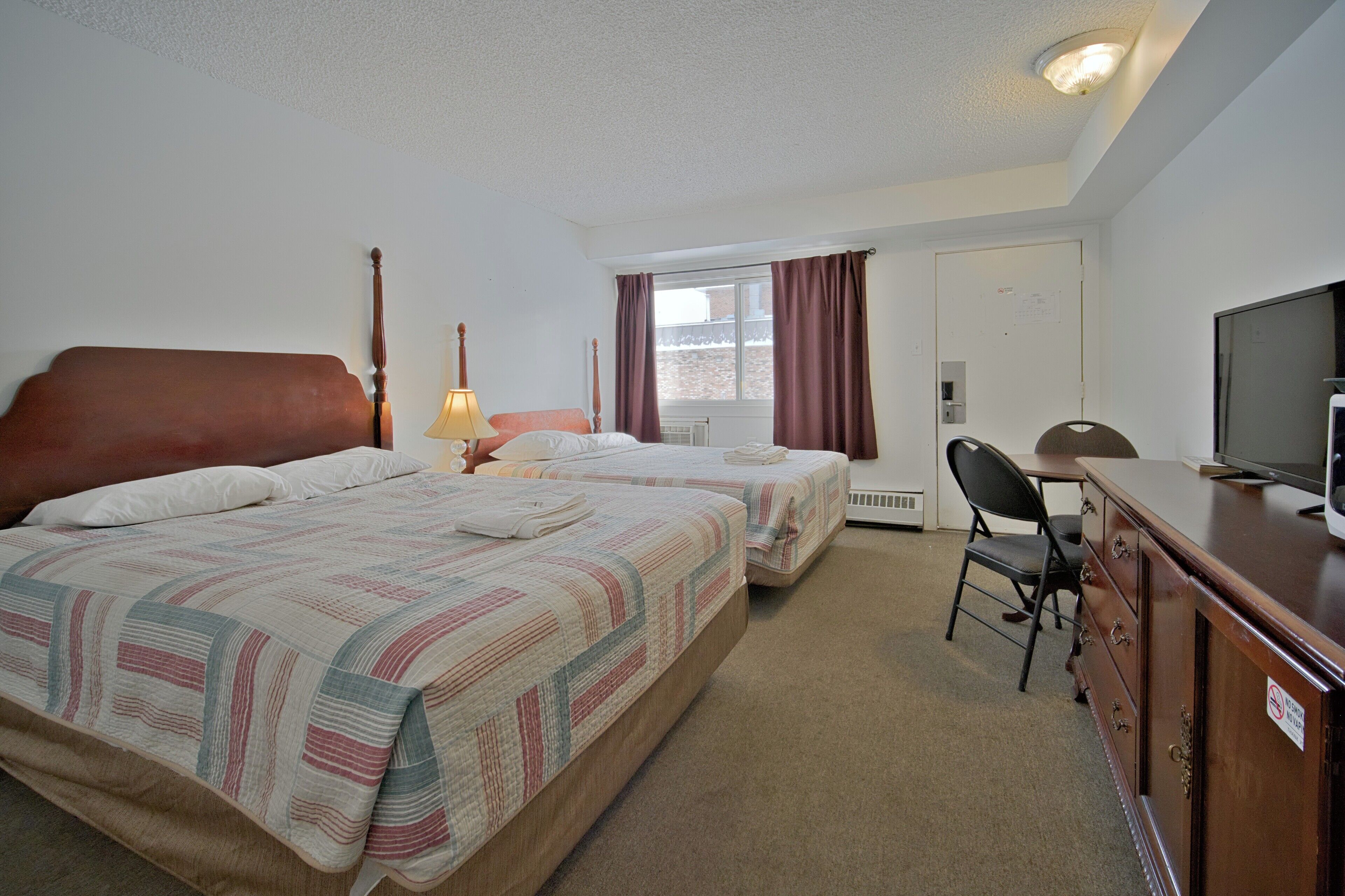 A hotel room with two beds, a desk, a television, and a chair.