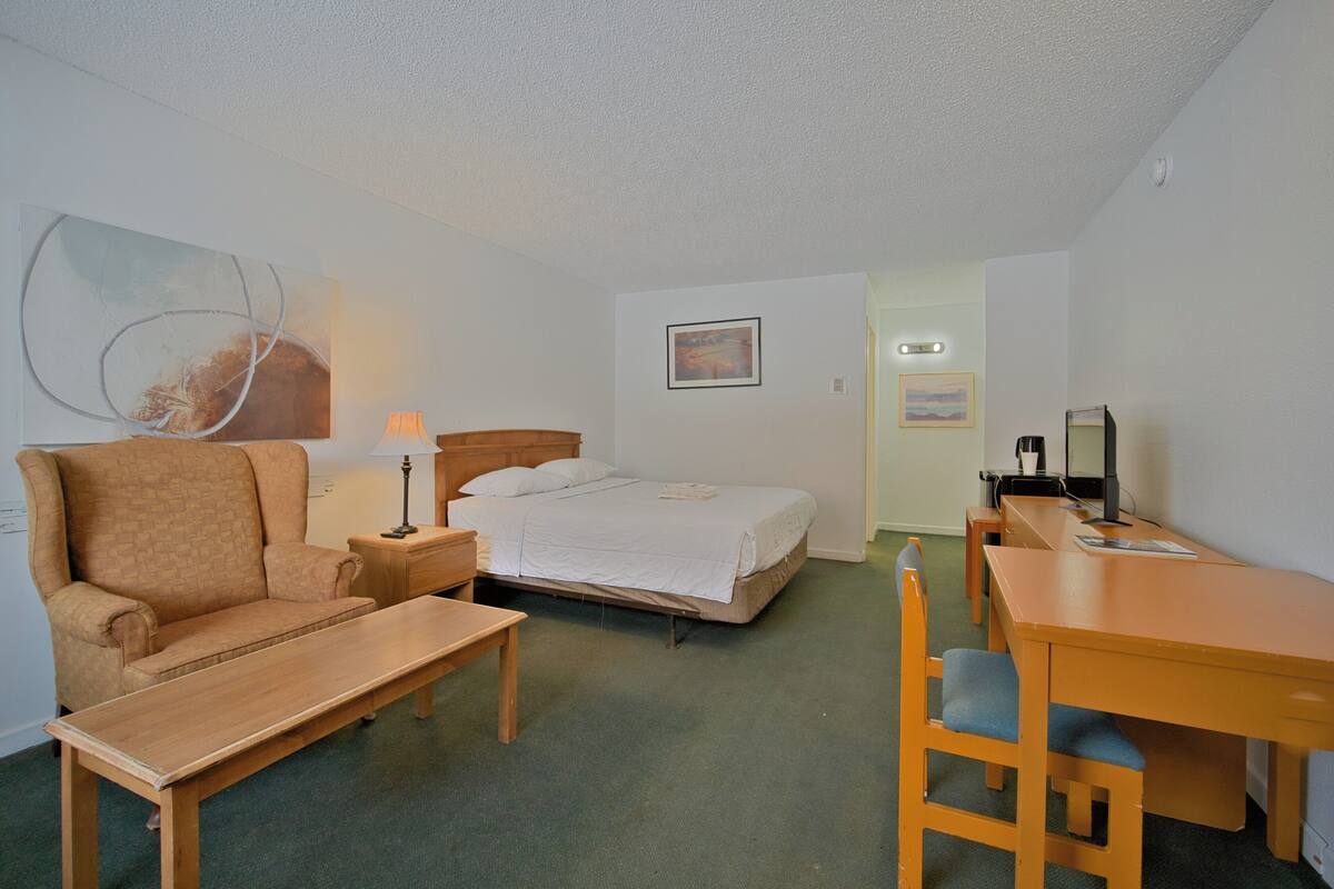 A hotel room with a bed, a chair, a desk, a lamp, and a painting on the wall.