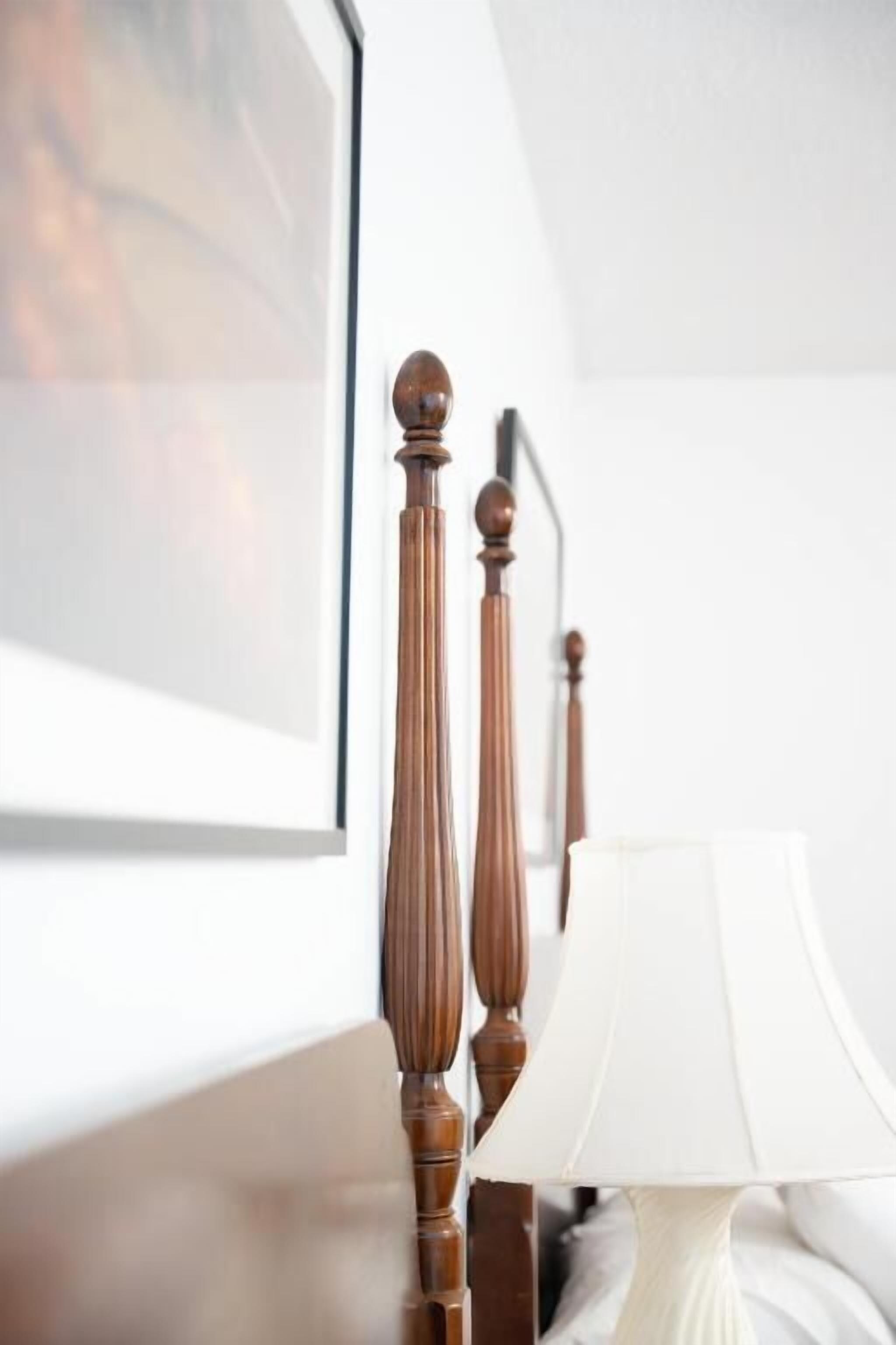 Un lit avec une tête de lit en bois, une lampe de chevet blanche et un tableau encadré accroché au mur.