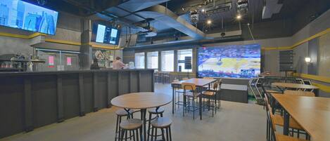 A modern restaurant interior with high ceilings, exposed ductwork, and a bar area with stools.