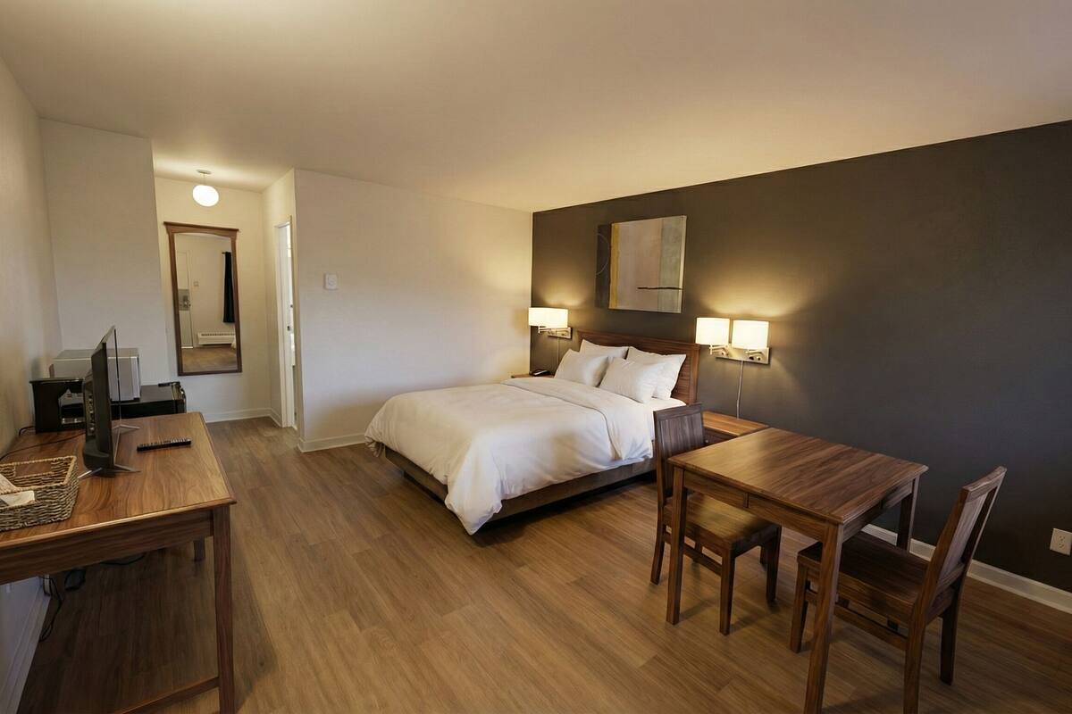 A hotel room with a bed, bedside table, desk, chair, and a wall-mounted lamp.