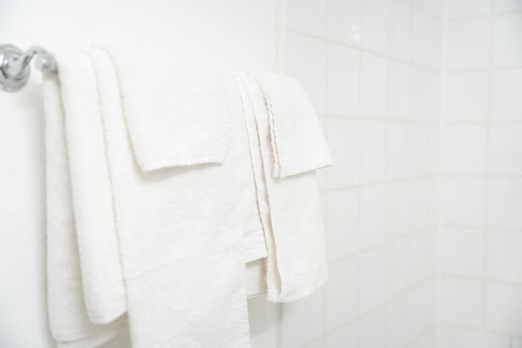 A bathroom with white tiled walls and a white towel hanging on a metal towel rack.