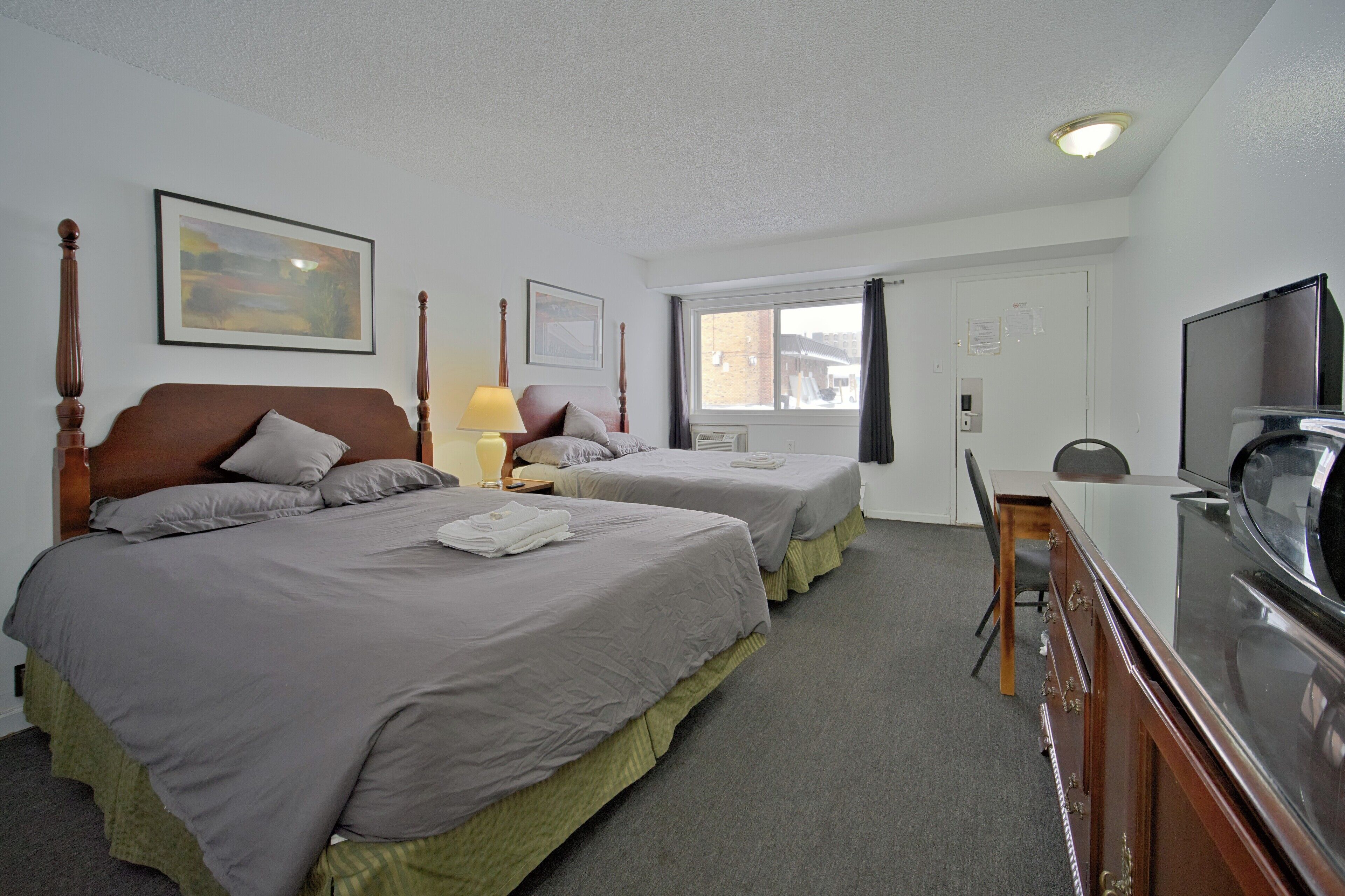 Ett hotellrum med två sängar, ett skrivbord, en tv och ett fönster med gardiner.