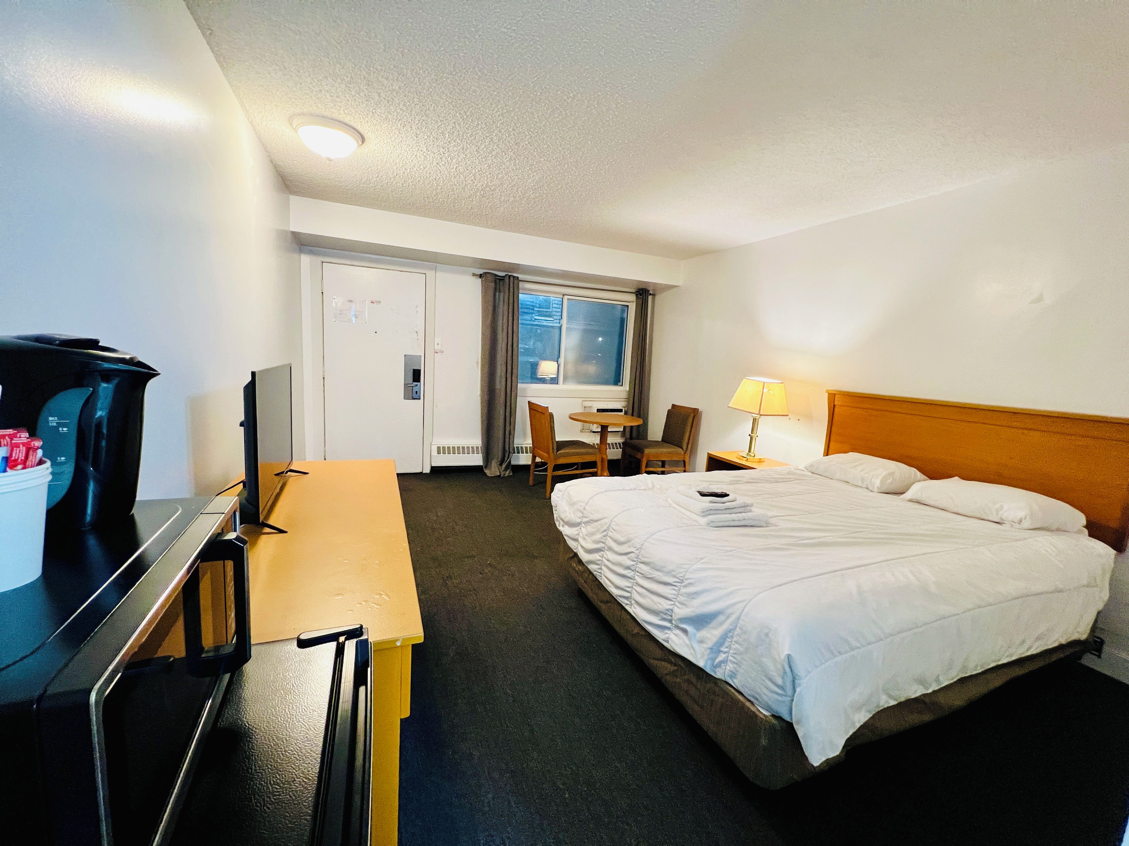 Una habitación de hotel con cama, escritorio, silla, televisor y ventana.