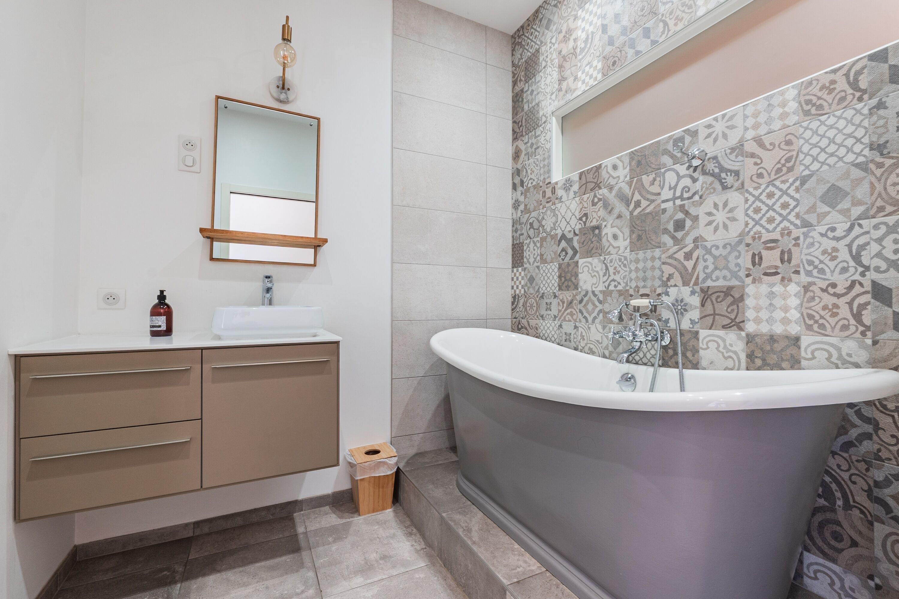 Un baño moderno con una bañera independiente, un tocador con espejo y azulejos estampados en las paredes.