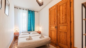 A bedroom with a bed, a wooden wardrobe, a nightstand with a lamp, and a window with curtains.