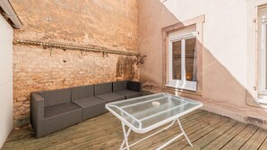 An outdoor patio with a glass-top table, a dark wicker sofa, and a wooden deck.