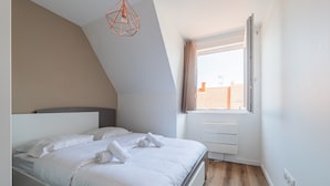 A bedroom with a bed, a window with curtains, a ceiling light fixture, and a view of the outside. - L'Escapade Strasbourgeoise - Magnifique petit T2 refait à neuf (Strasbourg)