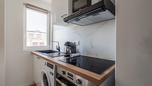 A compact kitchen with a built-in washing machine, a microwave, and a stovetop. - L'Escapade Strasbourgeoise - Magnifique petit T2 refait à neuf (Strasbourg)