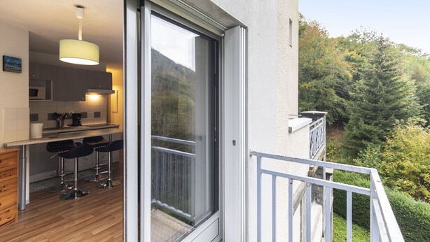 Een moderne keuken met een bar, een schuifdeur naar een balkon en uitzicht op een bebost gebied.
