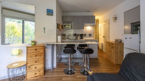 Een kleine keuken met een centraal eiland, barstoelen, een houten kast en een koelkast.
