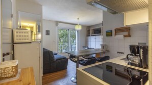 Een compacte keuken met een koelkast, magnetron en koffiezetapparaat. Er is een zithoek met een tafel en stoelen, en een bank. De keuken heeft een raam dat voor natuurlijk licht zorgt.