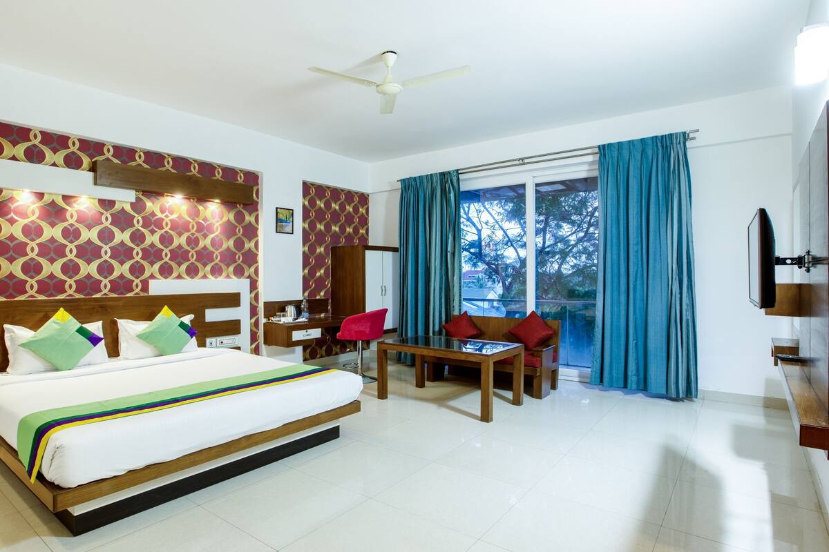 Habitación de hotel con cama, escritorio, silla, televisor y ventana con cortinas.