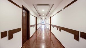 Un largo pasillo bien iluminado con puertas de madera y paredes blancas, que conduce a una habitación luminosa al final.