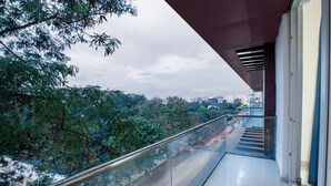 Un balcón con barandilla de vidrio que da a un paisaje urbano y zonas verdes.